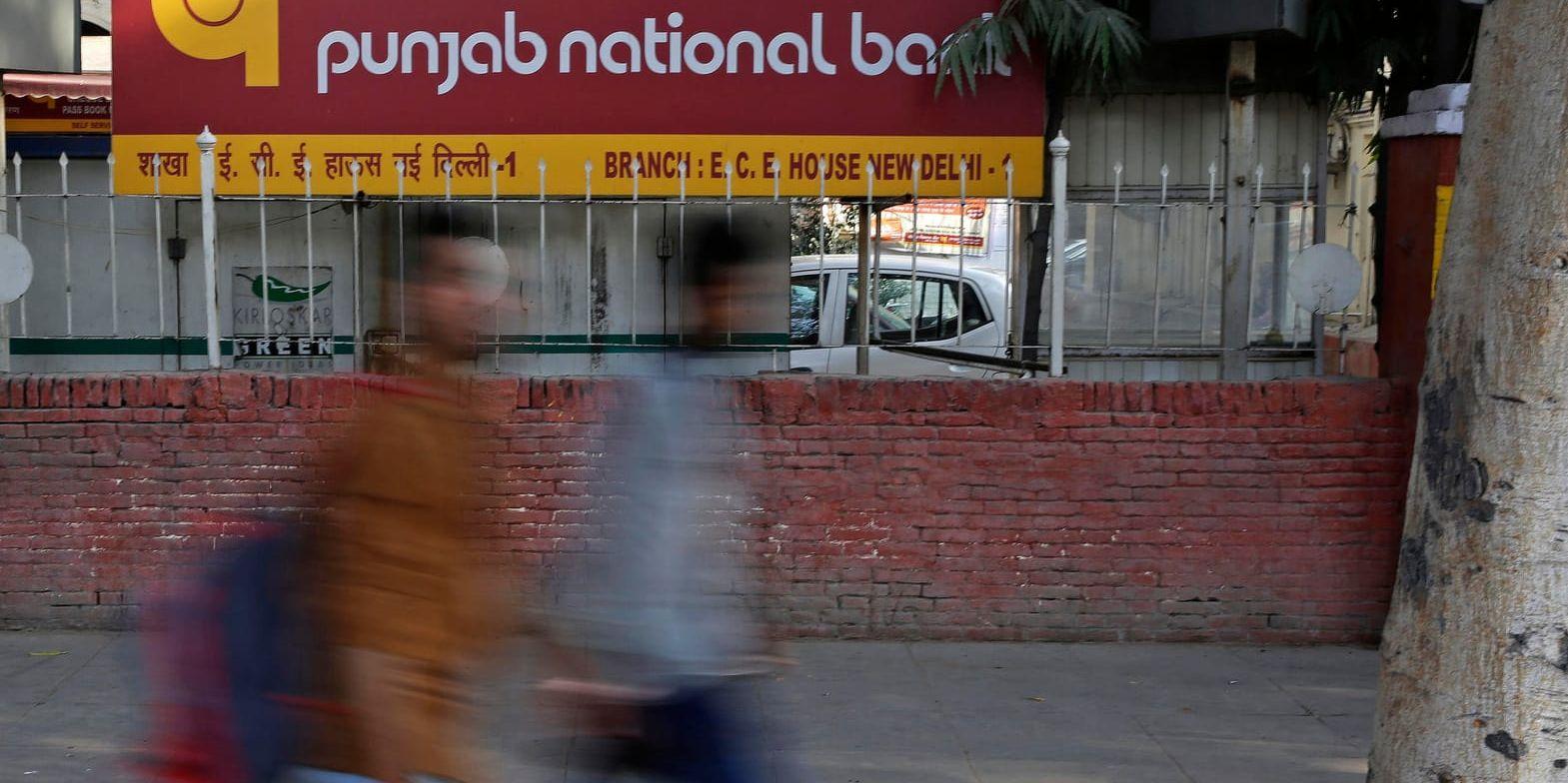Två anställda på Punjab National Bank i Indien misstänks ligga bakom den största bedrägerihärvan i landets historia. På bilden syns två personer passera en skylt med bankens namn i New Delhi. Bilden har ingen anknytning till artikeln.