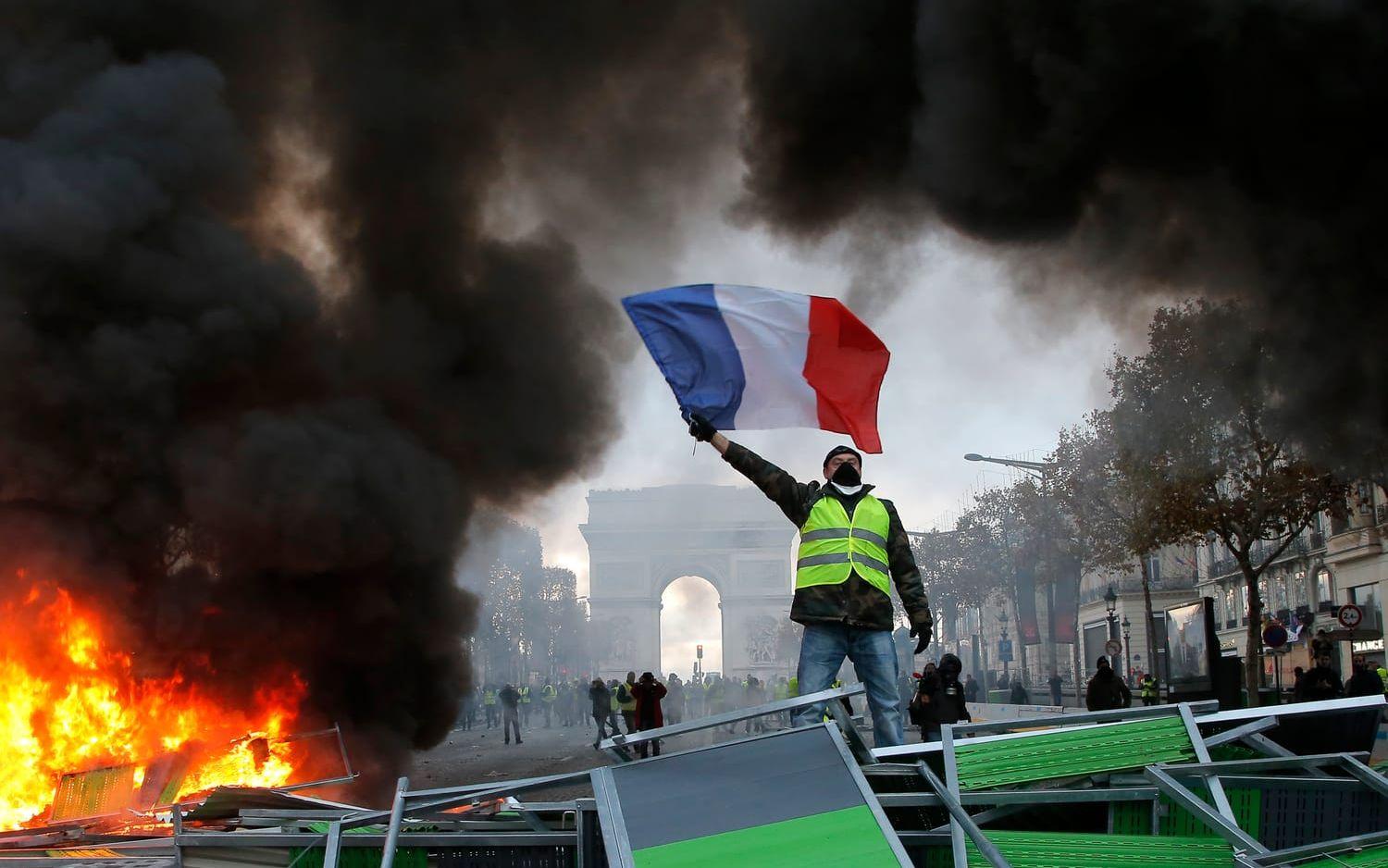 En demonstrant på paradgatan Champs-Élysées viftar med den franska flaggan.