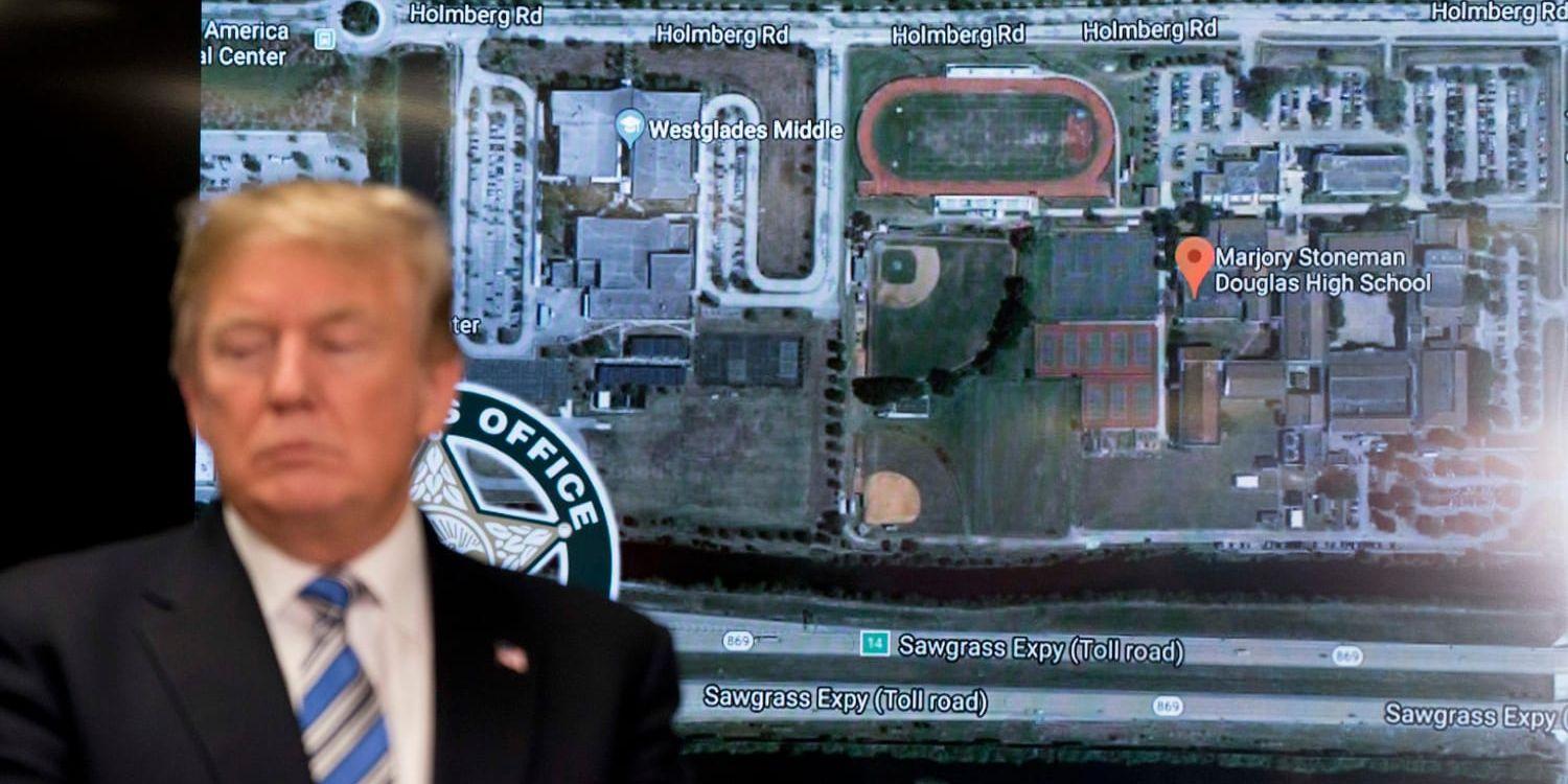 Donald Trump står framför ett flygfoto av skolan i Florida som drabbades av skolskjutningen.