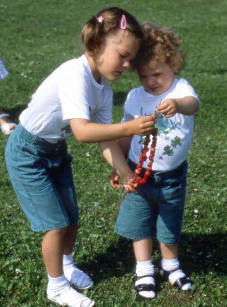 Assisterar lillebror. Victoria och Carl Philip trär smultron på strån, inför prinsessans 5-årsdag 1982. Foto: Hovet / TT / AP
