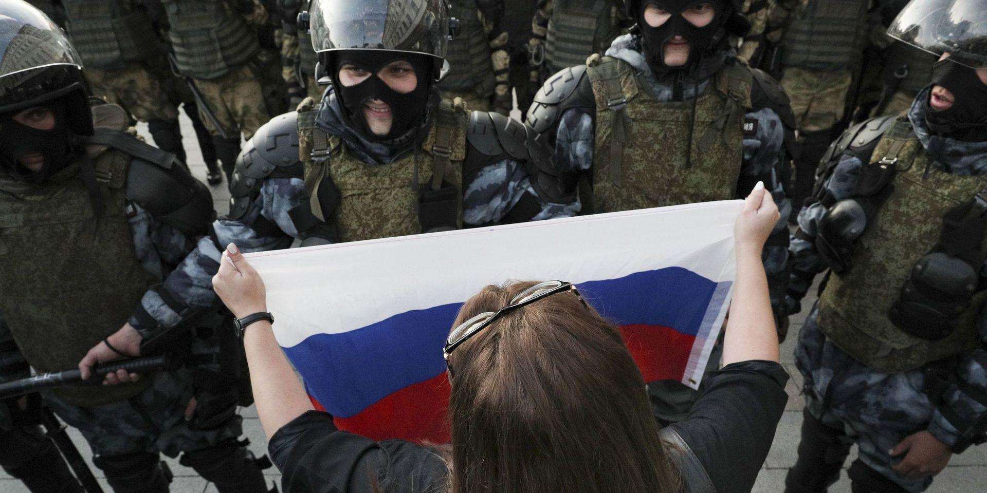 En kvinna håller upp ryska flaggan framför en grupp poliser under en demonstration i Moskva lördagen 10 augusti, när tusentals personer demonstrerade för tredje helgen i rad för att protestera ot att oberoende kandidater inte tillåts ställa upp i höstens borgmästarval .