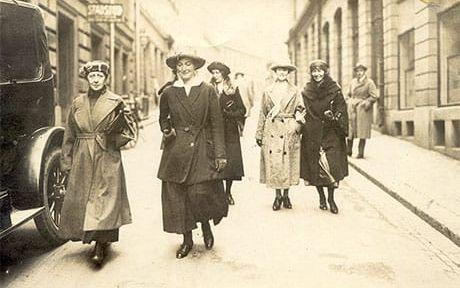 Eva Andén (1886-1970) som går i mitten i svart kappa var Sveriges första kvinnliga advokat. Hennes sambo och kollega Lisa Ekedahl går bakom längst till höger, klädd i svart. Kvinnorna är på väg att rösta den 16 september 1921.