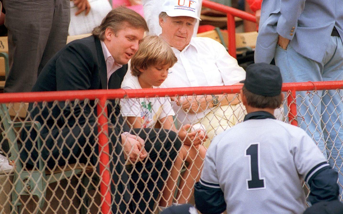 <strong>26 mars, 1988: </strong>Med sonen Donald Trump Jr på baseboll-match mellan Yankees och Montreal Expos. I handen håller sonen en boll som han just mottagit lagets tränare tränare Billy Martin. Till höger i bild syns också Yankees ägare George Steinbrenner. Foto: AP Photo/Richard Drew
