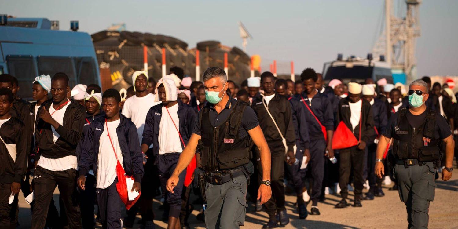 Italiensk gränspolis eskorterar flyktingar till ett mottagningscenter sedan de i midsommarhelgen satts i land på Sicilien av den spanska frivilligorganisationen Proactiva Open Arms.