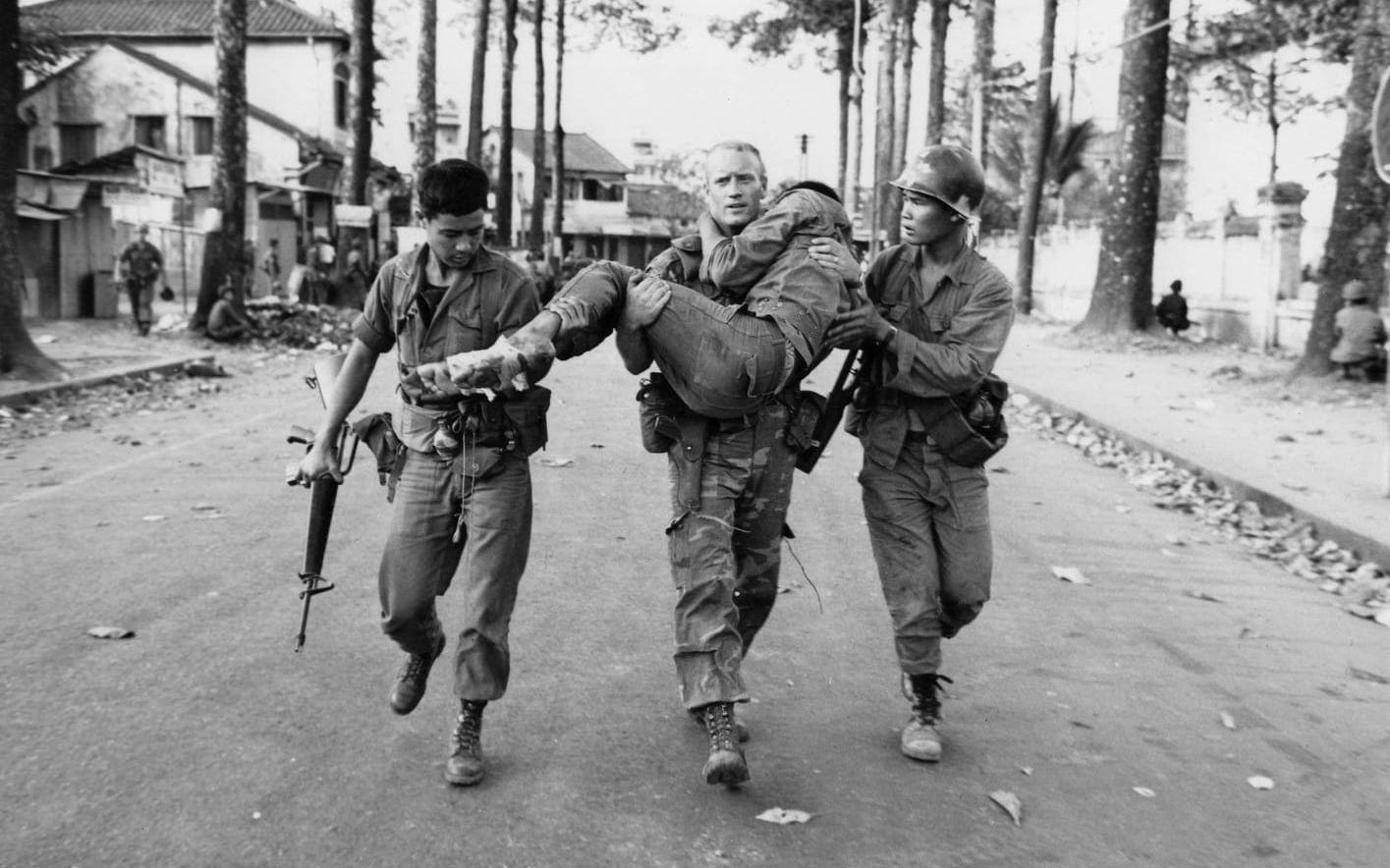 Den amerikanske löjtnanten Gary Jackson bär en sårad sydvietnamesisk soldat i säkerhet under striderna i Saigon under Tetoffensiven, 6 februari 1968. Arkivbild
