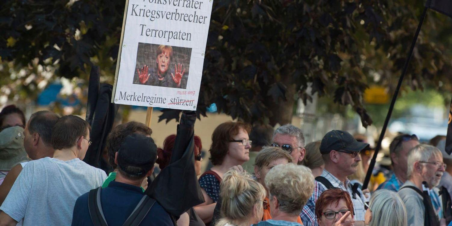 Demonstranter håller upp plakat med ett foto av Angela Merkel och texten "Förrädare, krigsförbrytare terroristgudmor – Merkelregeringen måste bort" i samband med Merkels besök i Dresden.