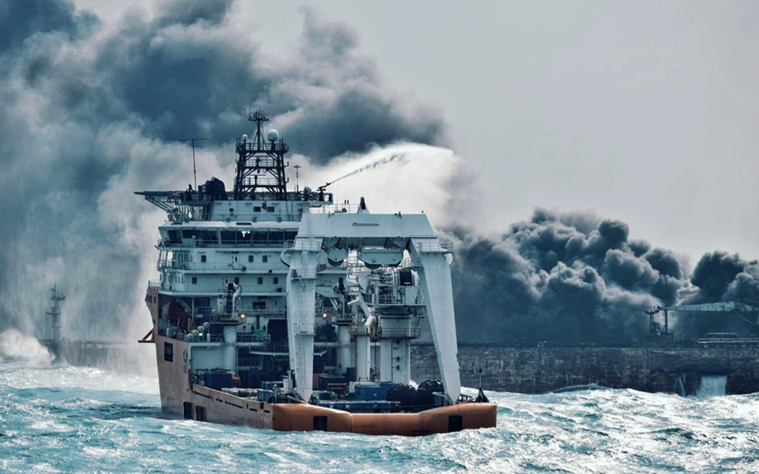 En räddningsbåt bekämpar branden på fartyget som har varit på drift mellan Kinas östra kust upp mot Japans södra kust under mer än en vecka. Bild: AP. 