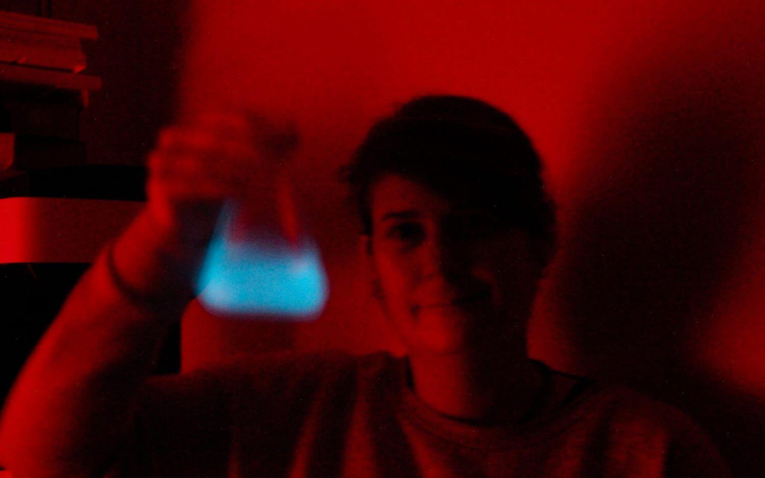 Miljontals mikroalger lyser upp när forskaren Kristie Rigby skakar en odling i det mörka laboratoriet.
