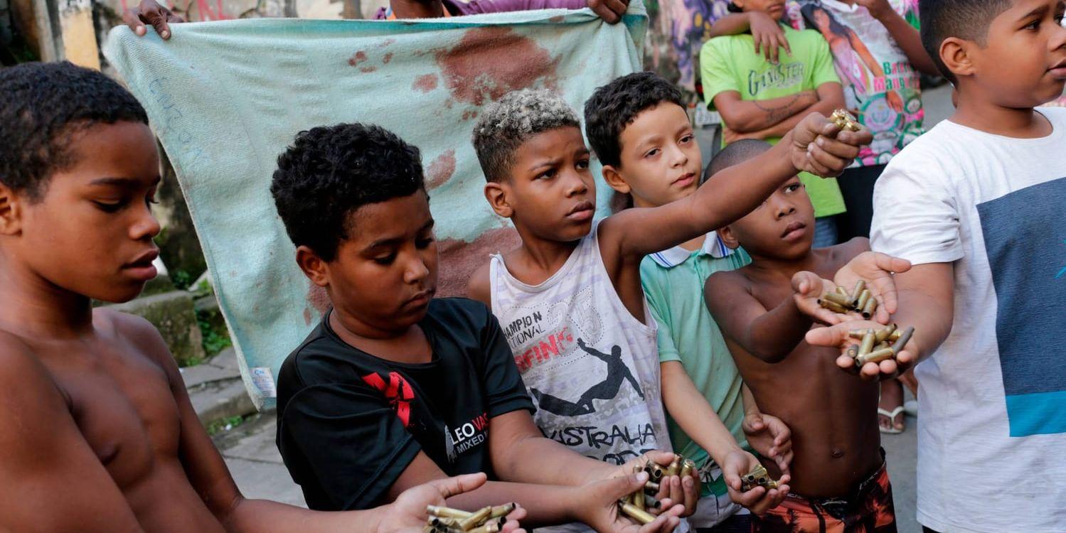 Barn visar upp använda patronhylsor och en blodig handduk efter att en 76-årig kvinna och hennes dotter som försökte hjälpa henne, dödats i en skottväxling mellan polis och knarkgäng i favelan Mangueira i Rio de Janeiro i slutet av juni.