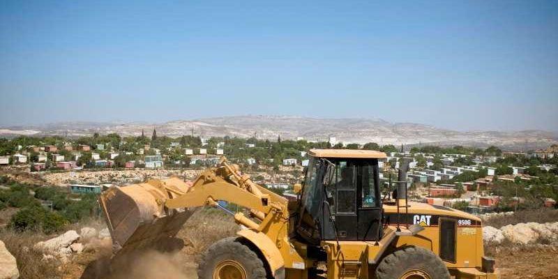 En grävskopa fraktar bort jord vid en bosättning i Ariel på Västbanken.

