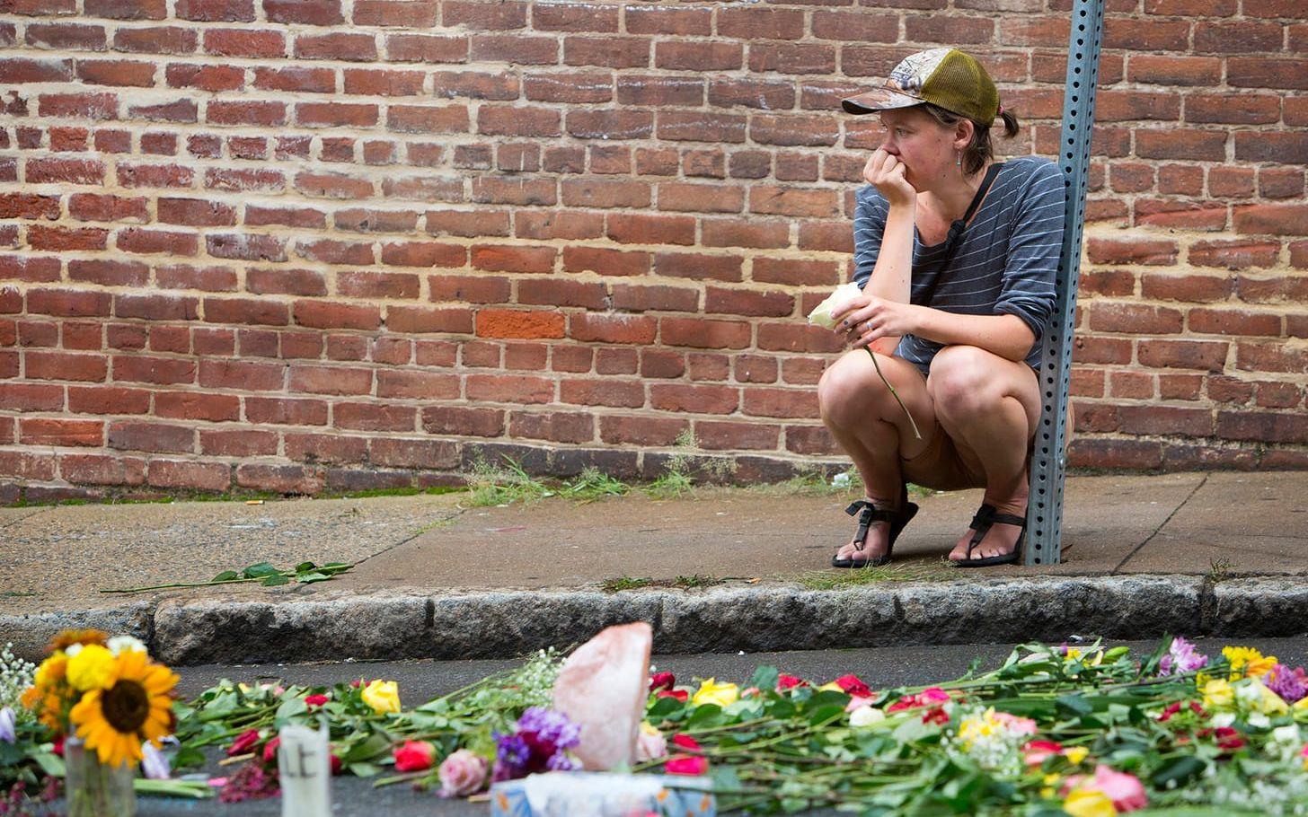 En kvinna sitter vid den plats som en kvinna kördes ihjäl på under oroligheterna i Charlottesville. FOTO: TT
