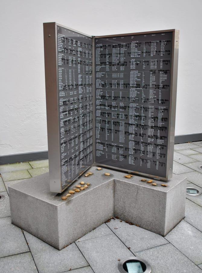 På judiska församlingens innergård finns två mörkt gråblå monument i slipad granit, "ett monument som konkret tydliggör att Förintelsen inte tog slut 1945, utan ett trauma som går i arv, fortsätter verka i såväl människor, i samhället", skriver Karin Brygger.  Bild: Dorothy Wild Braun