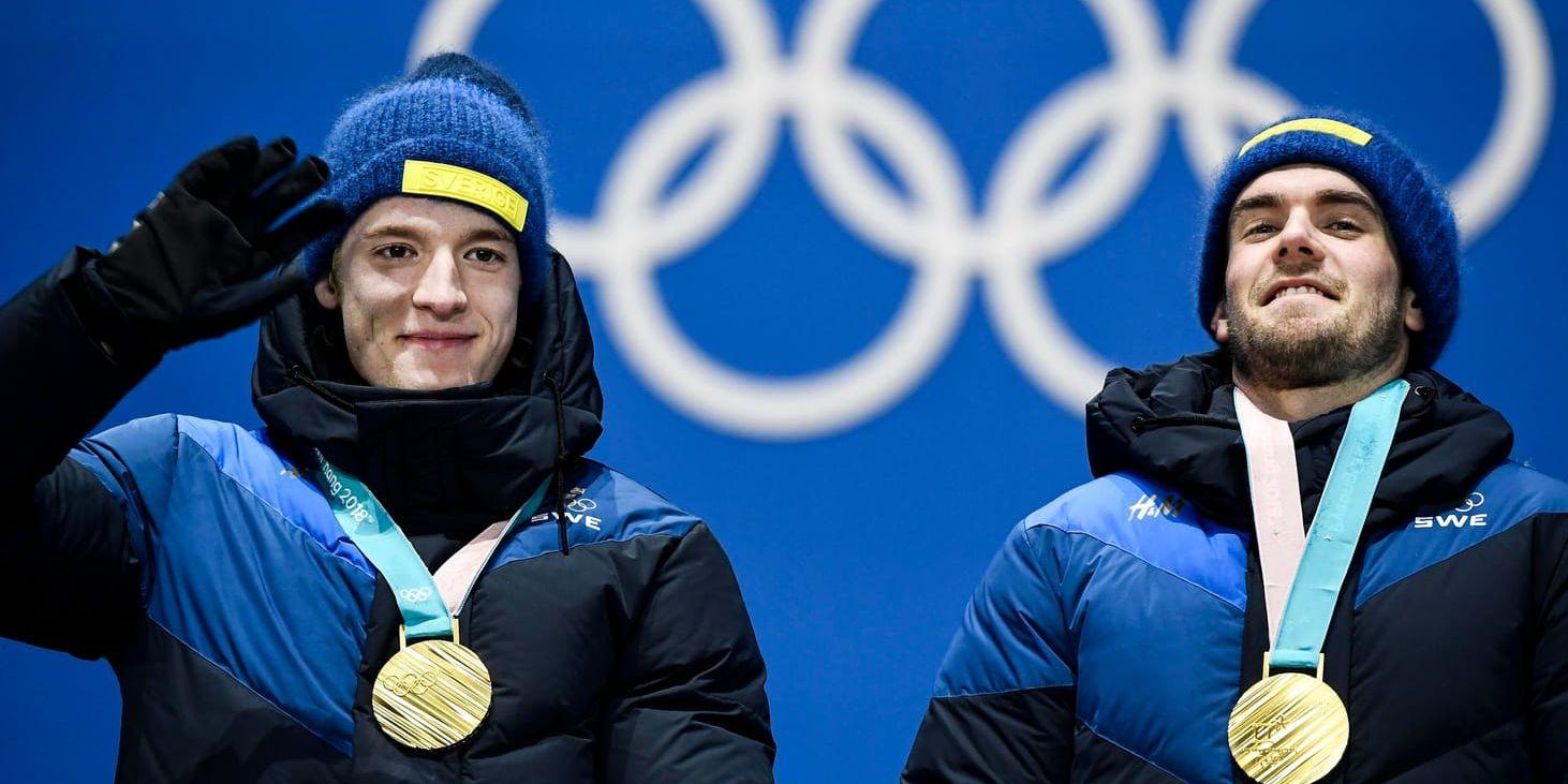 De svenska skidskyttarna Sebastian Samuelsson och Fredrik Lindström med sina OS-guldmedaljer under medaljceremonin för herrstafetten.