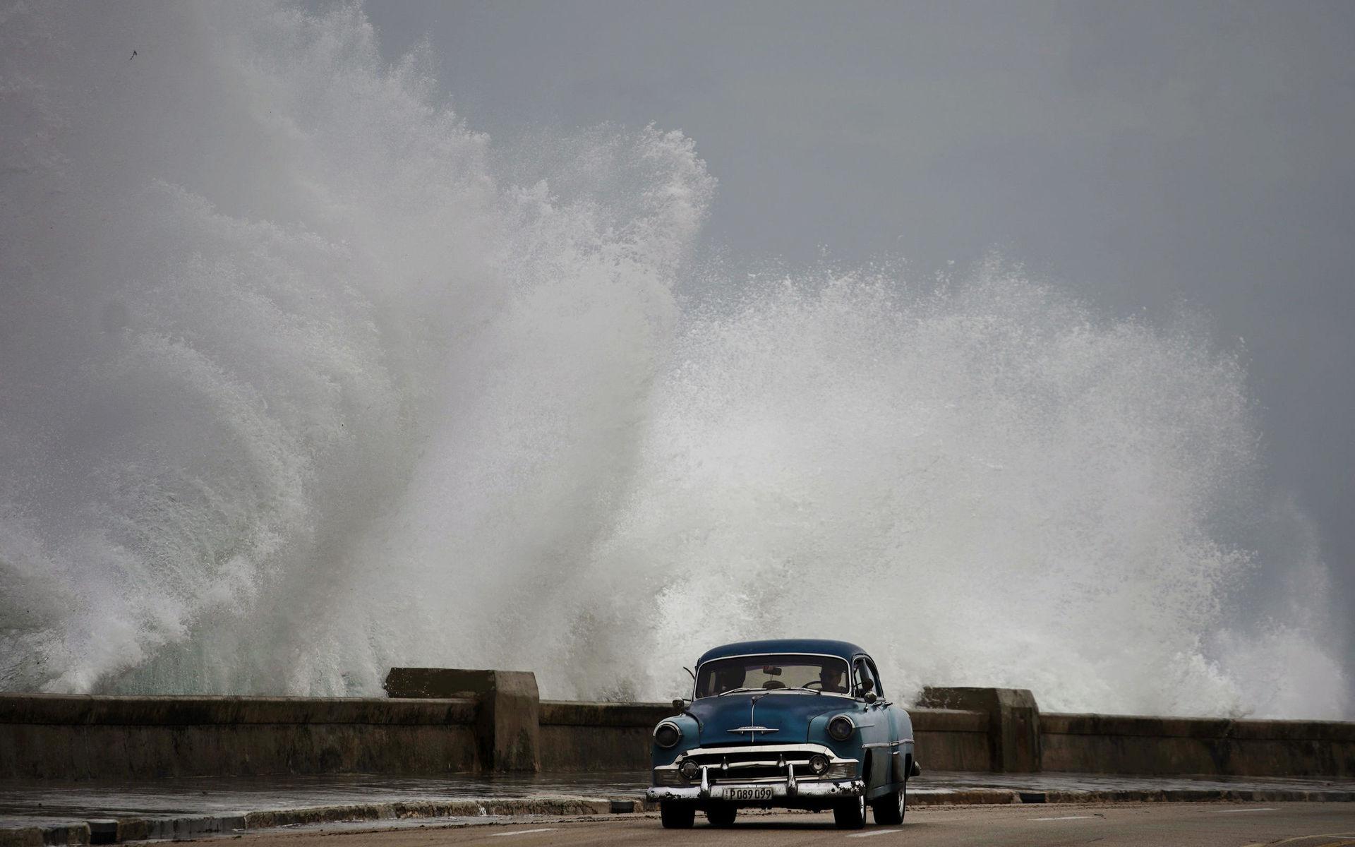 Vågorna slår in mot en klassisk amerikansk bil på Kuba.