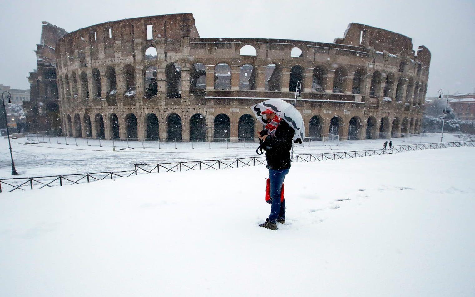 Man med paraply i snö utanför Colosseum i Rom.