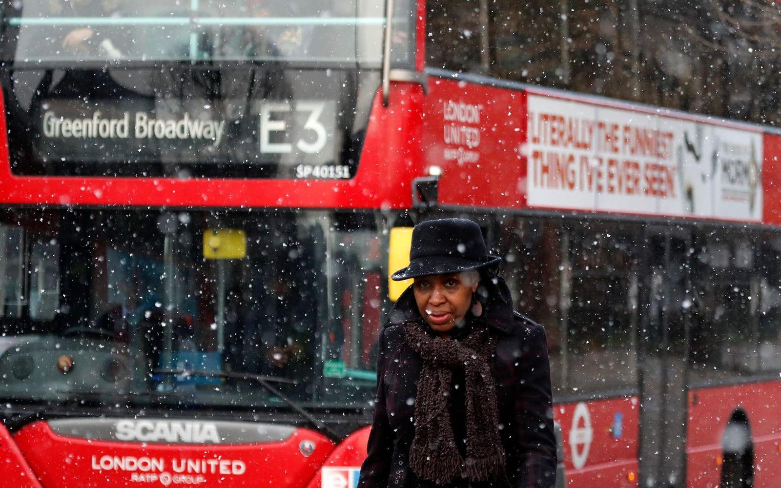 Kvinna i snöfall vid dubbeldäckare i London. 