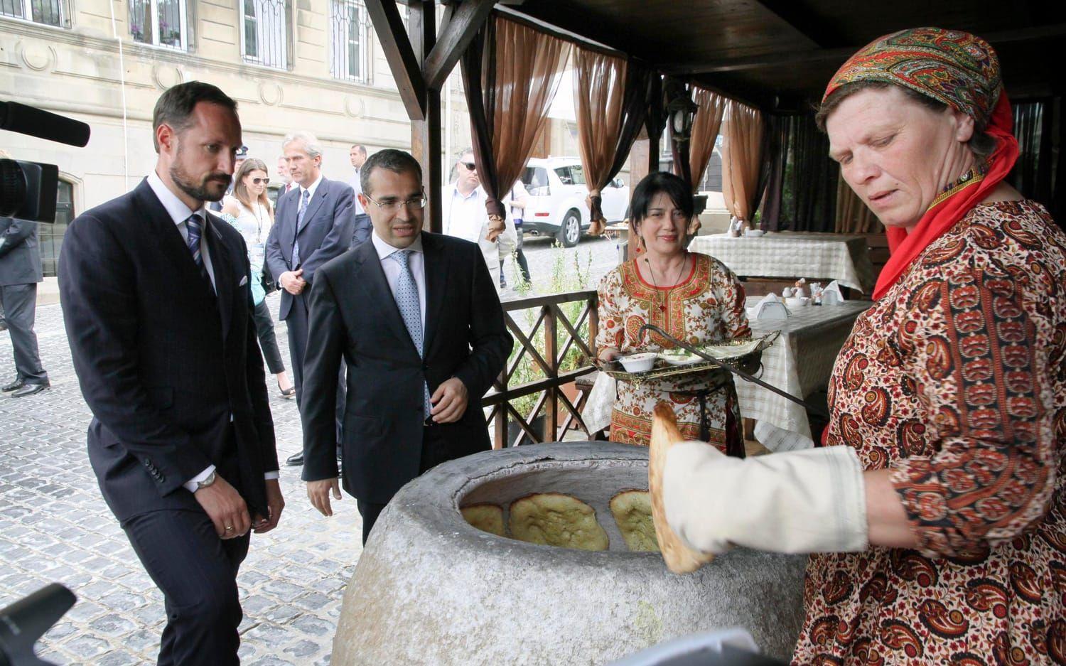Norges kronprins Haakon får testa det klassiska brödet bakat i den traditionella cylinderformade ugnen. Bild: TT.