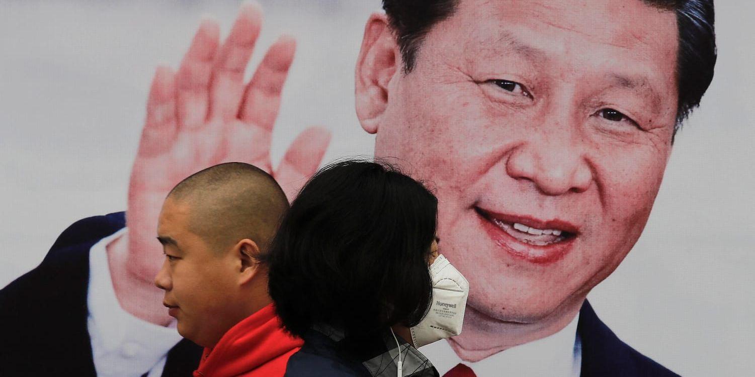 En kvinna och en man går förbi en affisch på Kinas president Xi Jinping. Arkivbild.