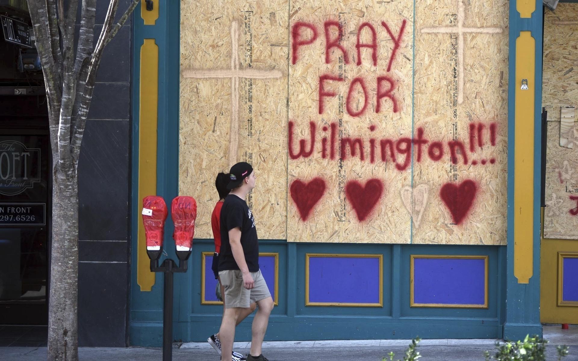 Människor går förbi några igenspikade fönster i kuststaden Wilmington i North Carolina. 