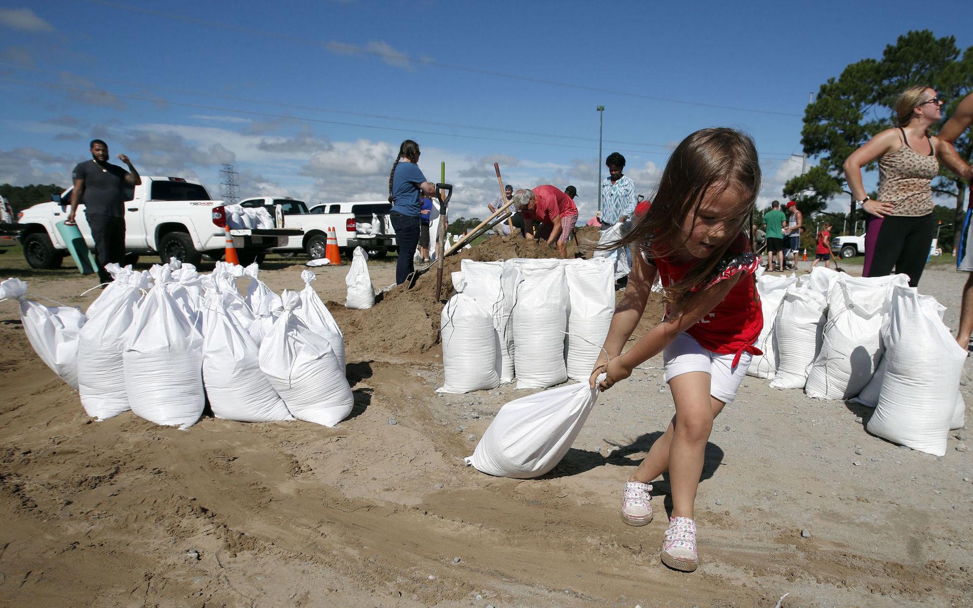 Chloe Heeden, 4, från Virginia Beach,drar en sandsäck mot sin pappas bil, i väntan på stormen. 