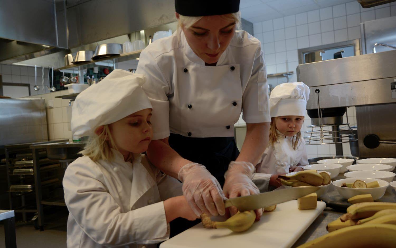 Dorotea Bollgård, kock på Eriksgårdens förskola hjälper Caroline Åkesson och Stella Daltegen att göra i ordning mellanmålet. Bild: Karina Hansson