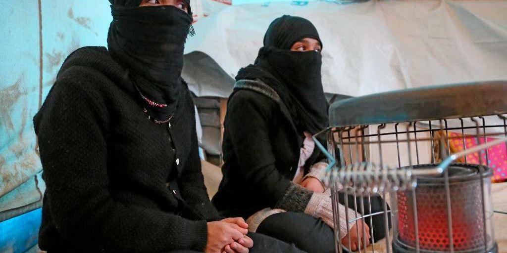 Yazidiska kvinnor värmer sig vid en kamin.
