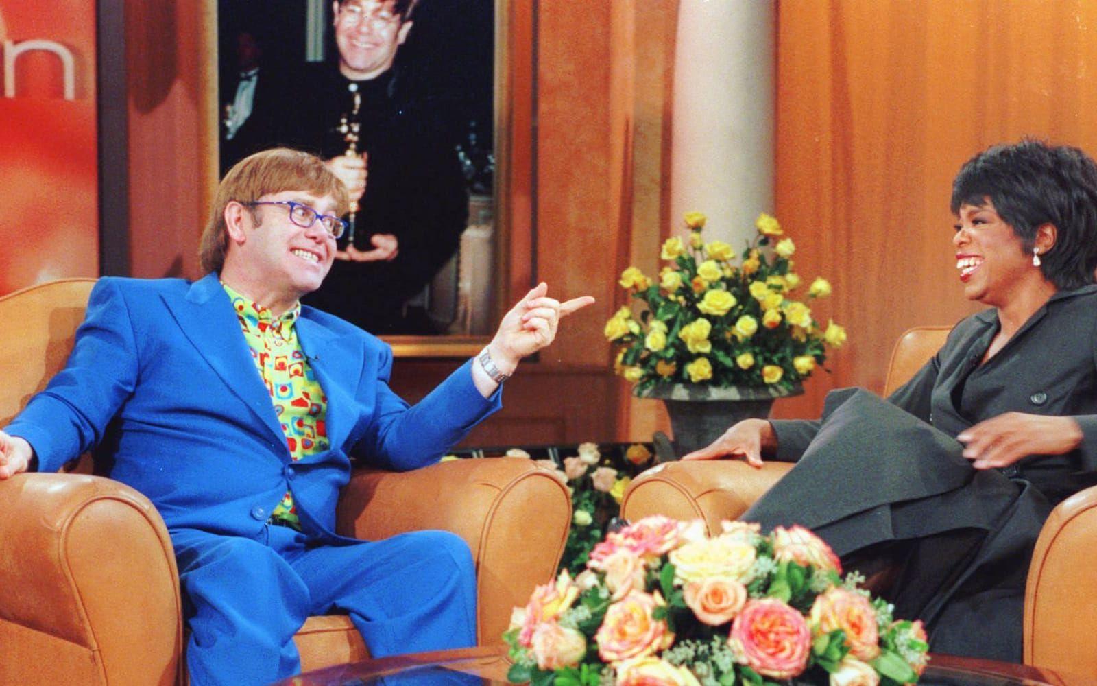 1997: Elton John gästar Oprah Winfreys talkshow. I bakgrunden skymtar vi Elton med Oscarn som han vann för ”Can you feel the love tonight” och ”Lejonkungen” 1994. Foto: TT
