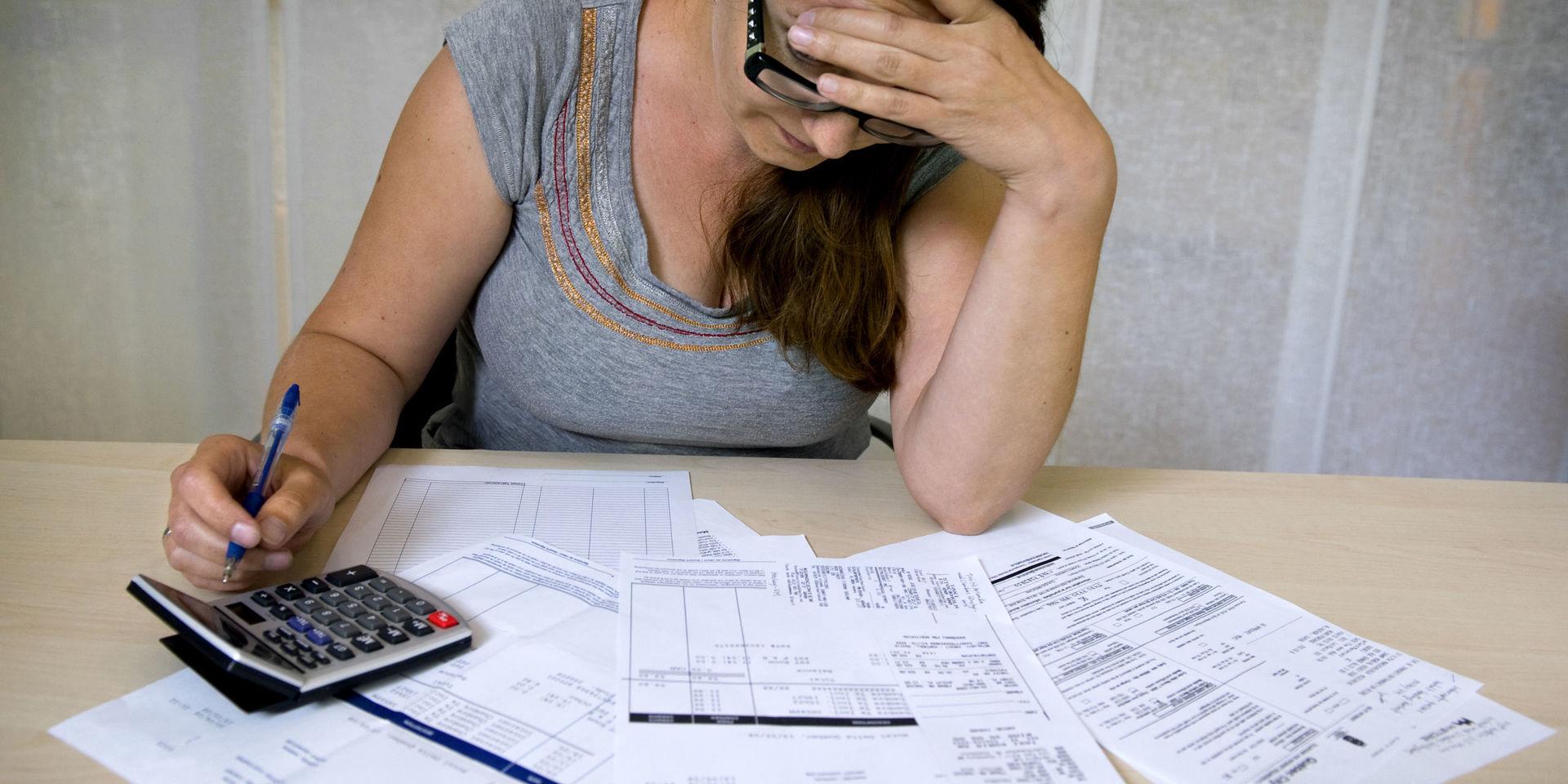 En skuldsatt kvinna sitter lutar över sina räkningar. Arkivbild.