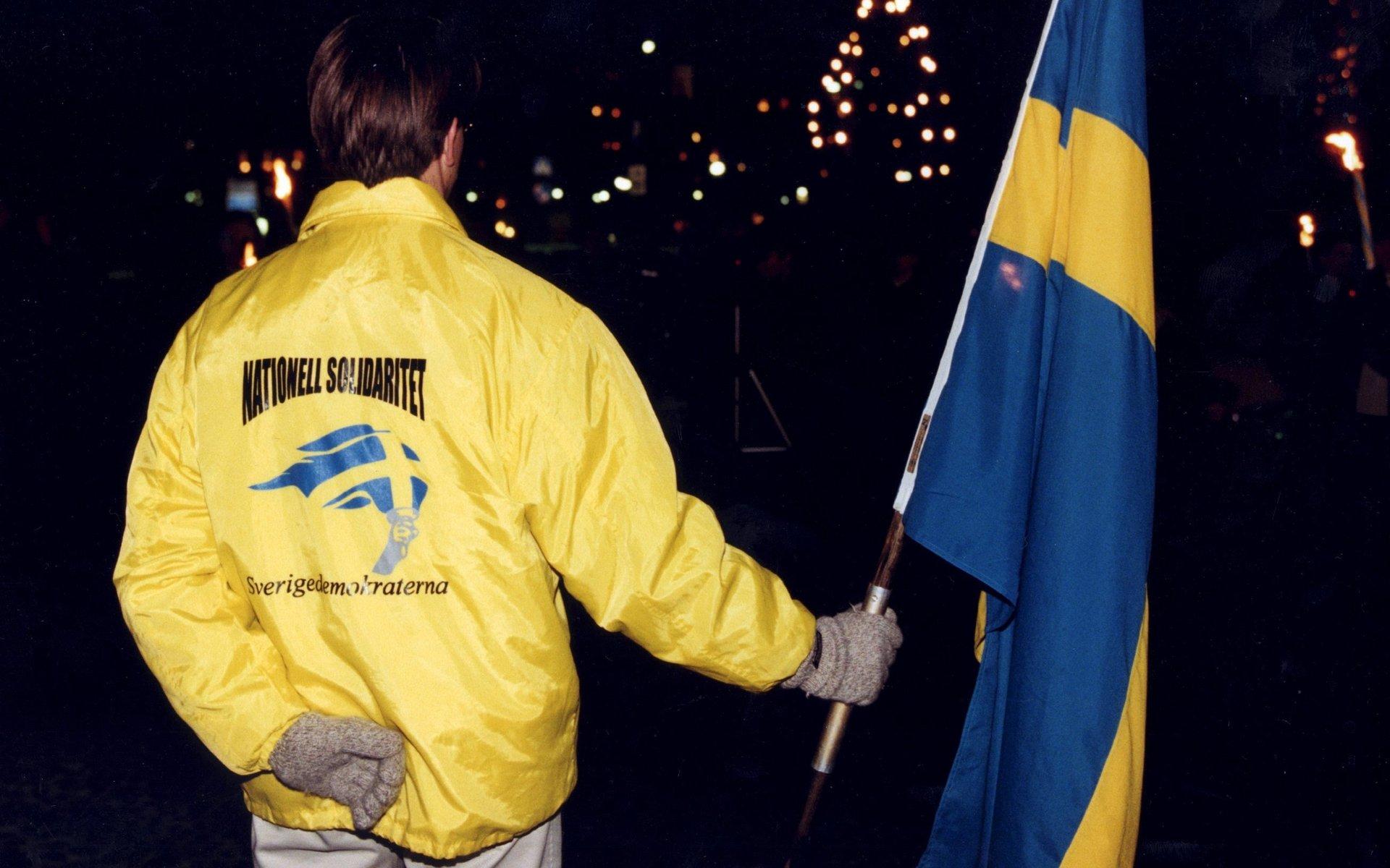 En Sverigedemokrat med svensk flagga och texten ”Nationell solidaritet” på ryggen vid en 30:e november-demonstration 1997. 