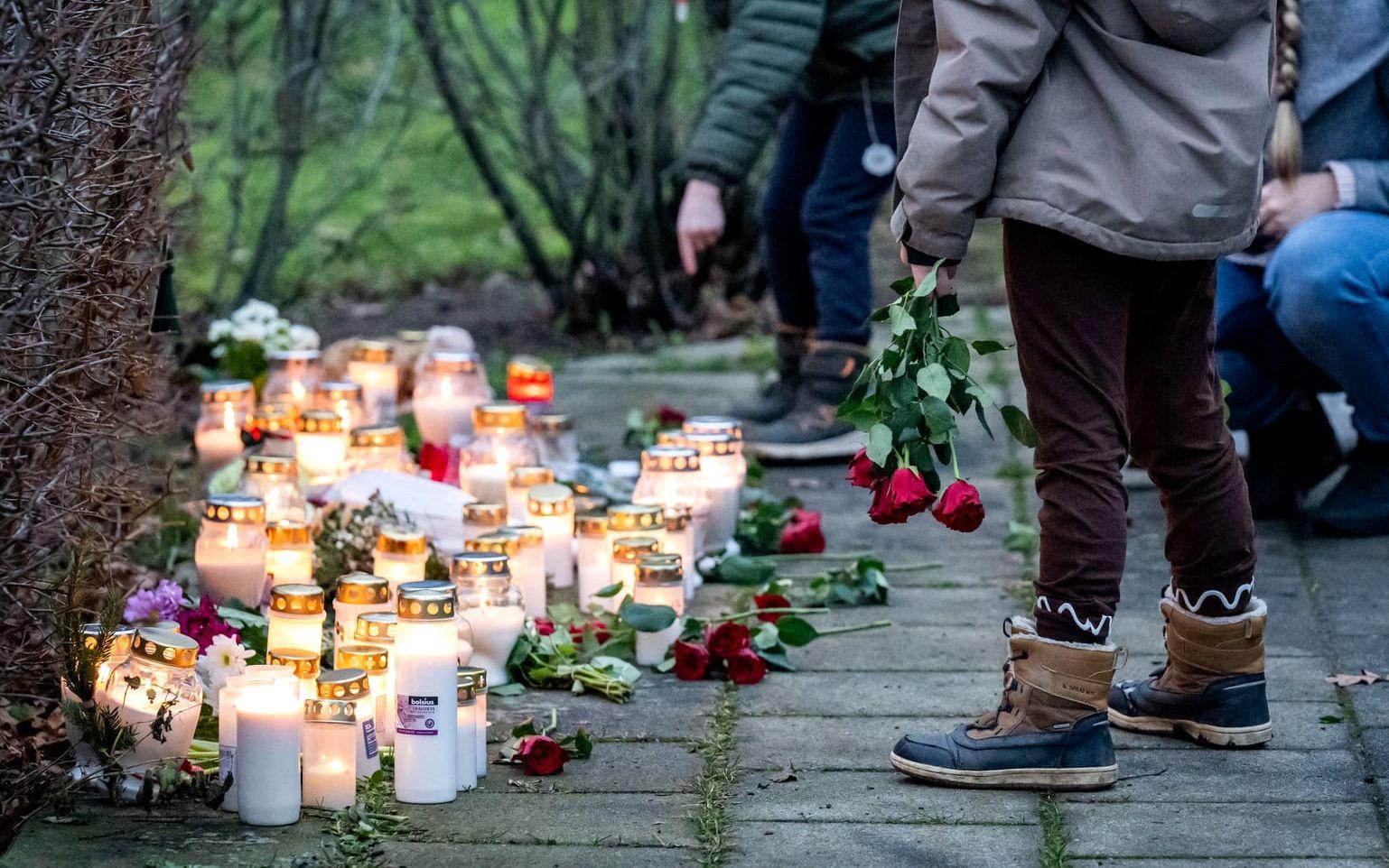Barn och vuxna lägger blommor och tänder ljus vid minnesplatsen utanför bostaden i Hörby där en kvinna och ett barn misstänks ha mördats. 