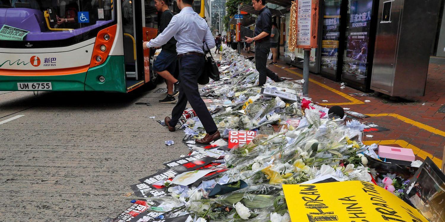 Pendlare går förbi blommor och skyltar som placerats vid en busshållplats efter en av jättedemonstrationerna i Hongkong.