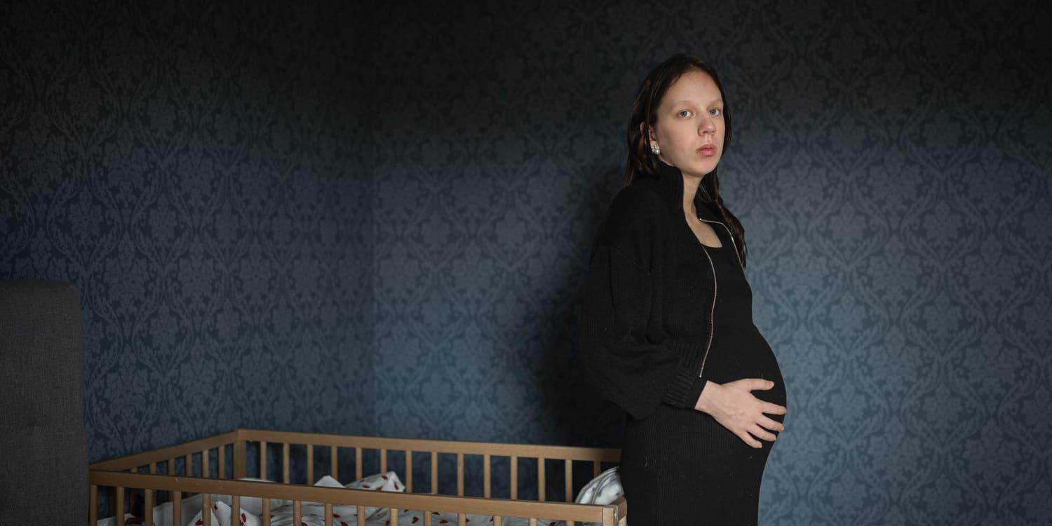 Linnea står bredvid en barnsäng, med en graviditetsmage, i mörkt rum.