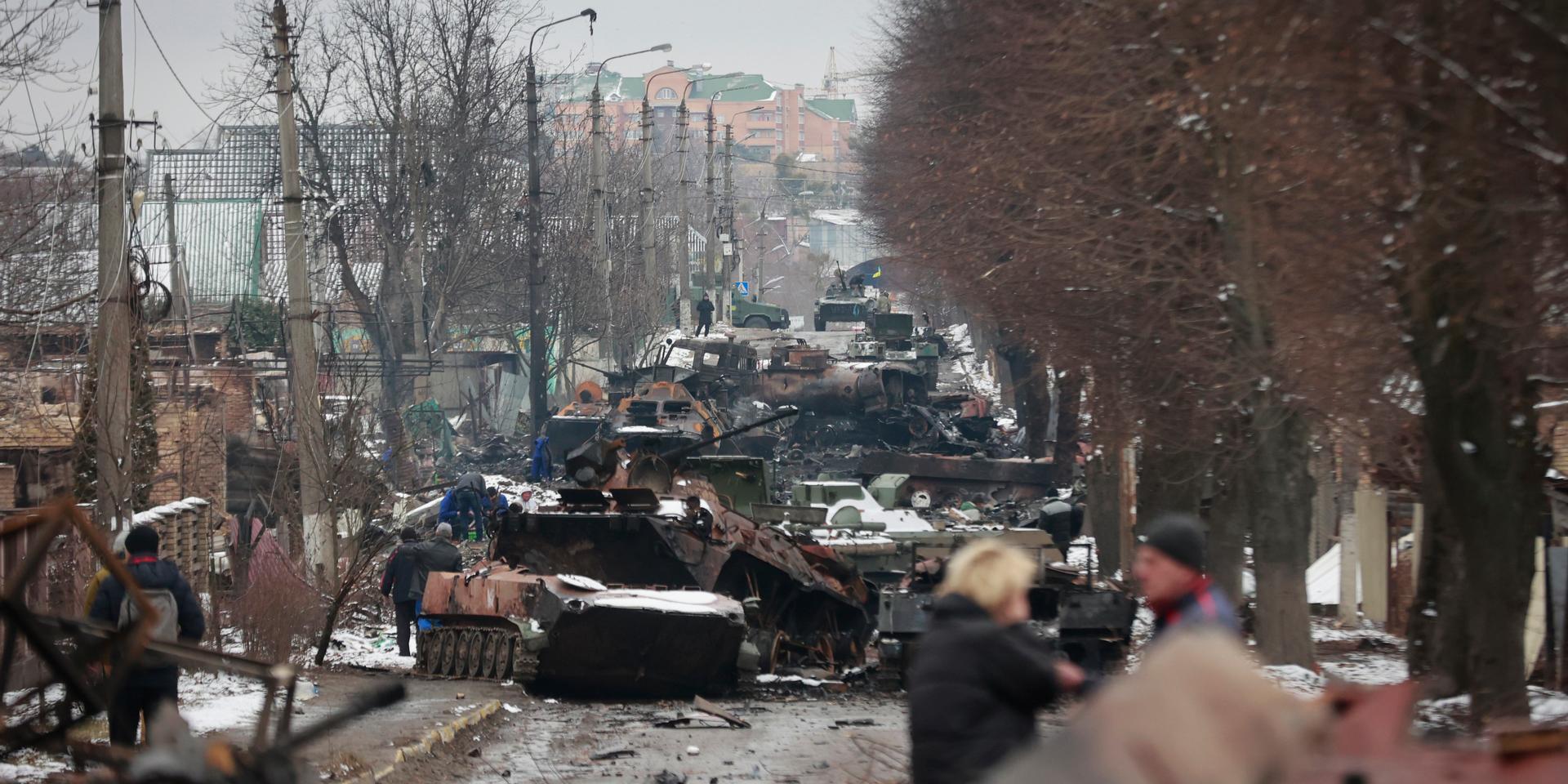 Människor tittar på förödelsen av ryska militära fordon på en väg i Butja utanför Kiev, i en bild från i tisdags.