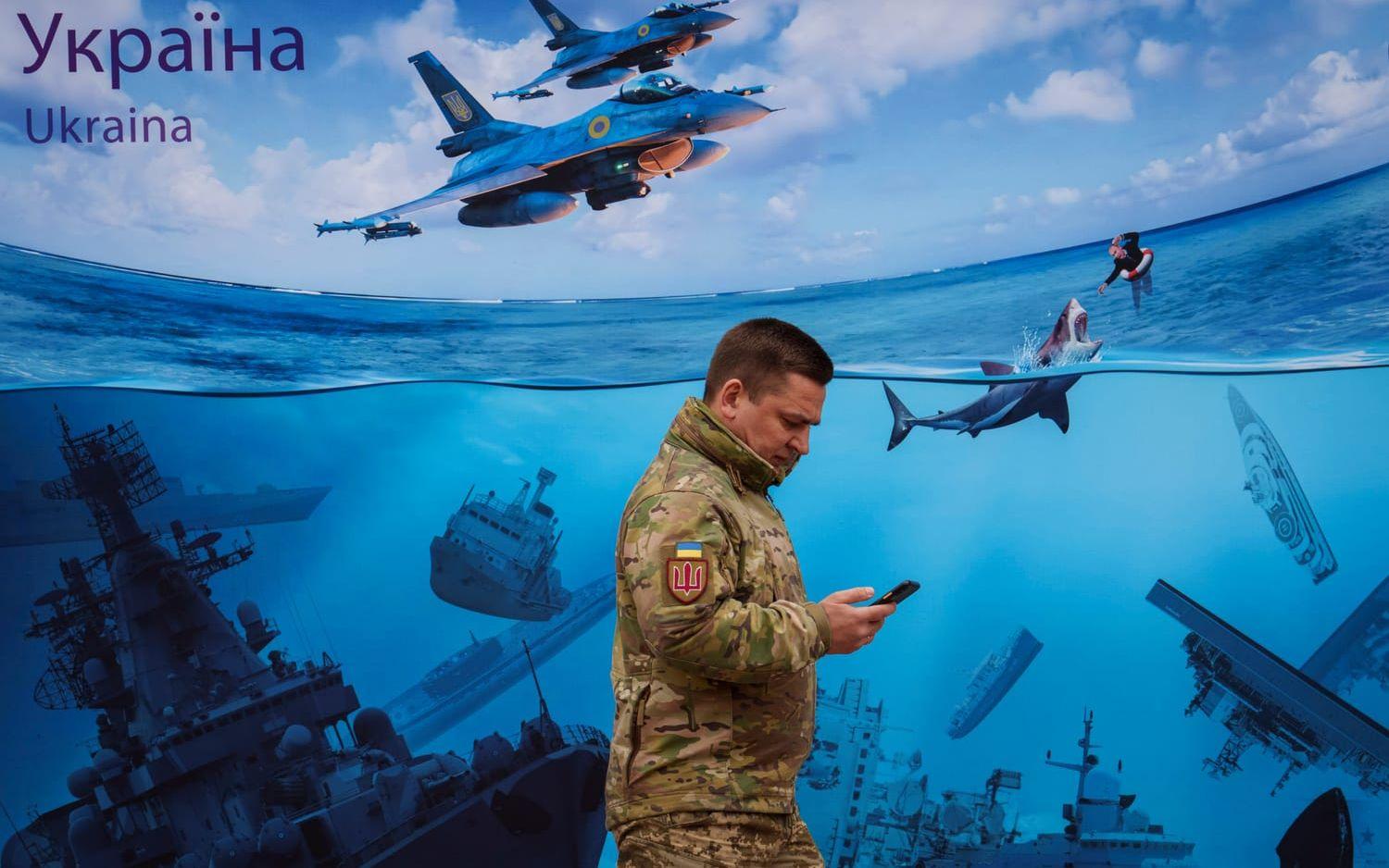 En ukrainsk soldat passerar en stor illustration som ska visa sänkta ryska örlogsfartyg och en Vladimir Putin i sjönöd, i Kiev den 15 mars i år.