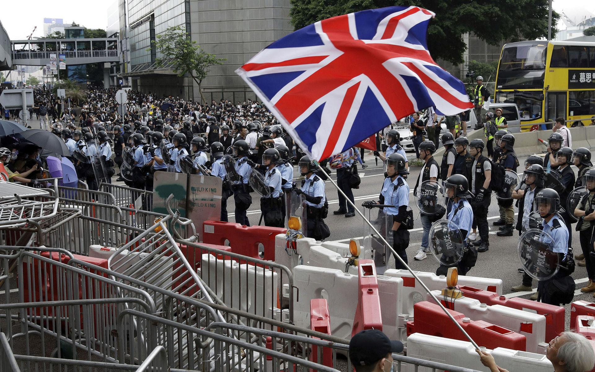 A man waves a British flag as policemen in anti-riot gear stand guard against the protesters on a closed-off road near the Legislative Council in Hong Kong, Wednesday, June 12, 2019. Hundreds of protesters surrounded government headquarters in Hong Kong on Wednesday as the administration prepared to open debate on a highly controversial extradition law that would allow accused people to be sent to China for trial. (AP Photo/Vincent Yu)