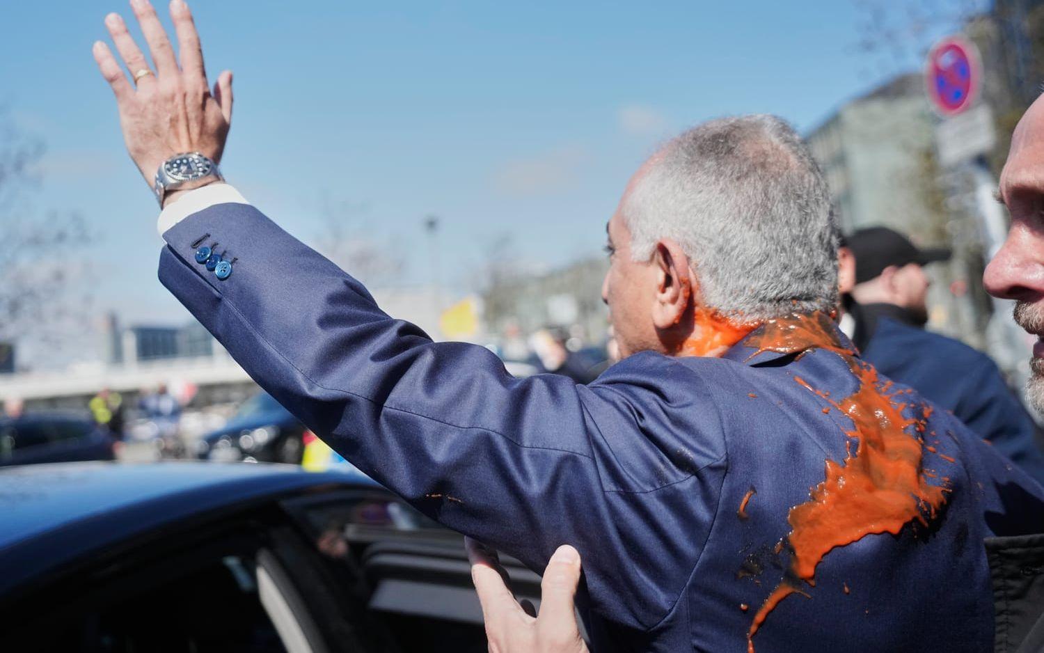 Reza Pahlavi vinkar till anhängare efter att han fått röd vätska kastad på sig efter en presskonferens i Berlin. 