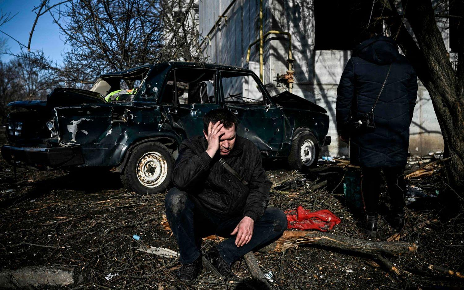 En man sitter utanför en förstörd byggnad efter bombningar i närheten av Charkiv i östra Ukraina.