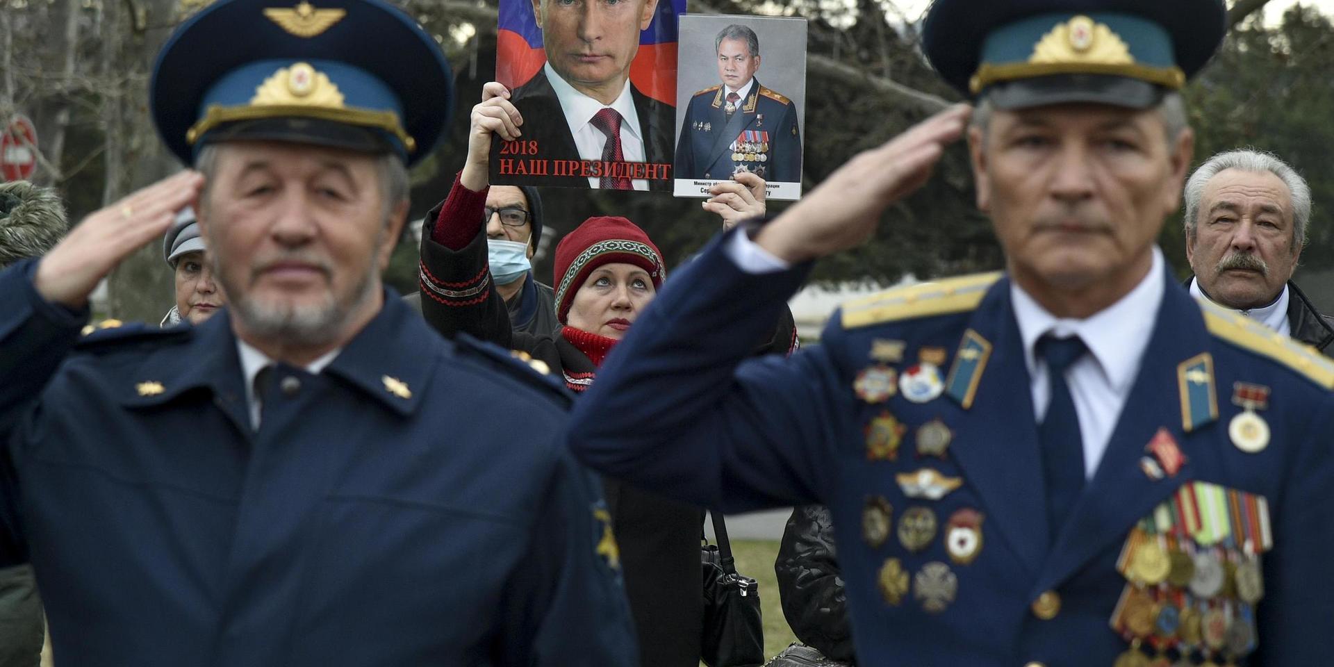 En kvinna håller upp porträtt av president Vladimir Putin och försvarsminister Sergej Shoigu bakom två militärveteraner vid en ceremoni i Sevastopol på Krim i vintras. Den ryska annekteringen är den viktigaste orsaken till spänningen med väst och Ryssland.