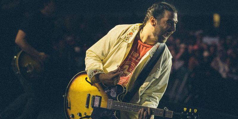 Noah Kahan sportar linnekostym och gitarr. 