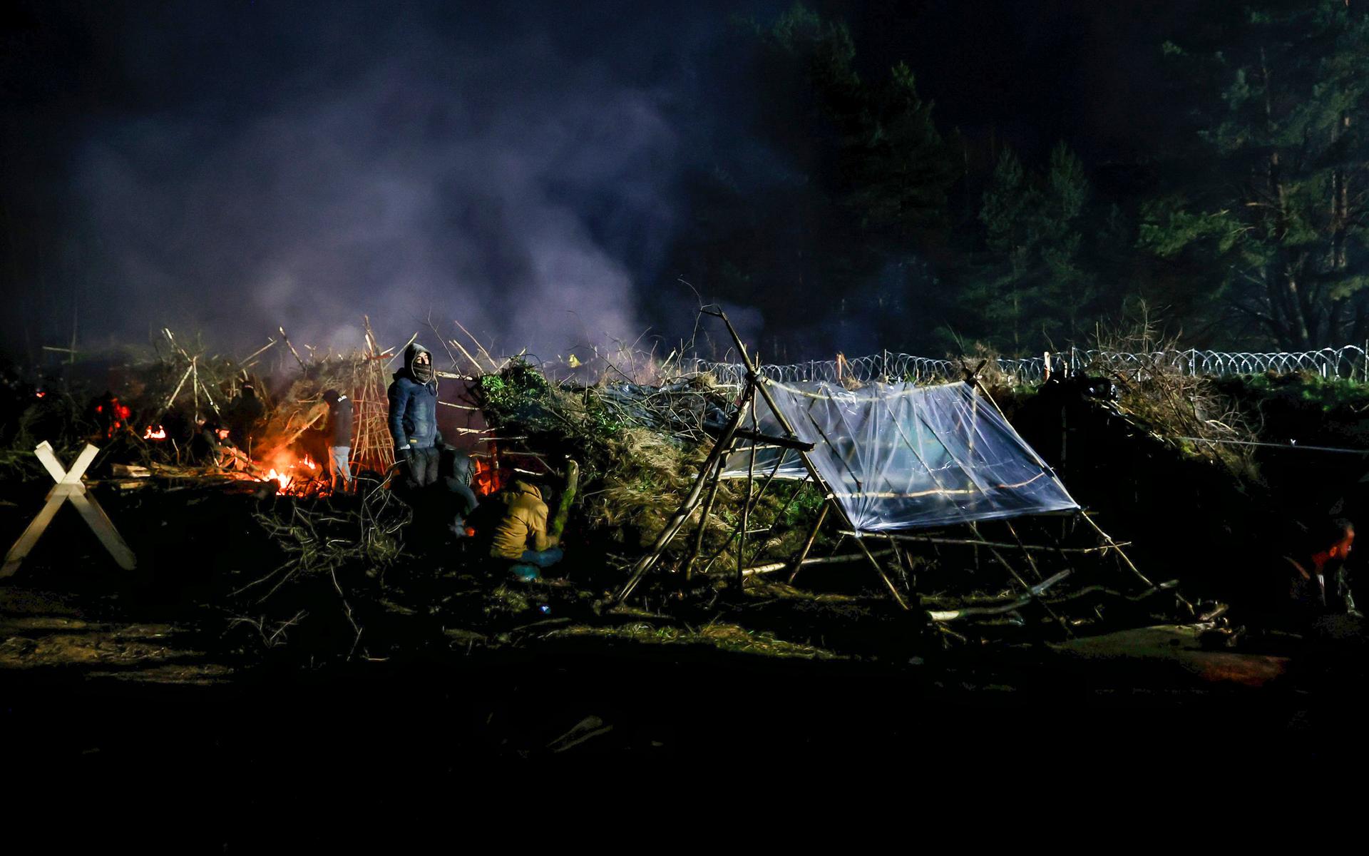 Kylan lägger sig nattetid över skogarna vid gränsen. Migranterna värmer sig vid en eld i ett tältläger nära Grodno, Belarus.