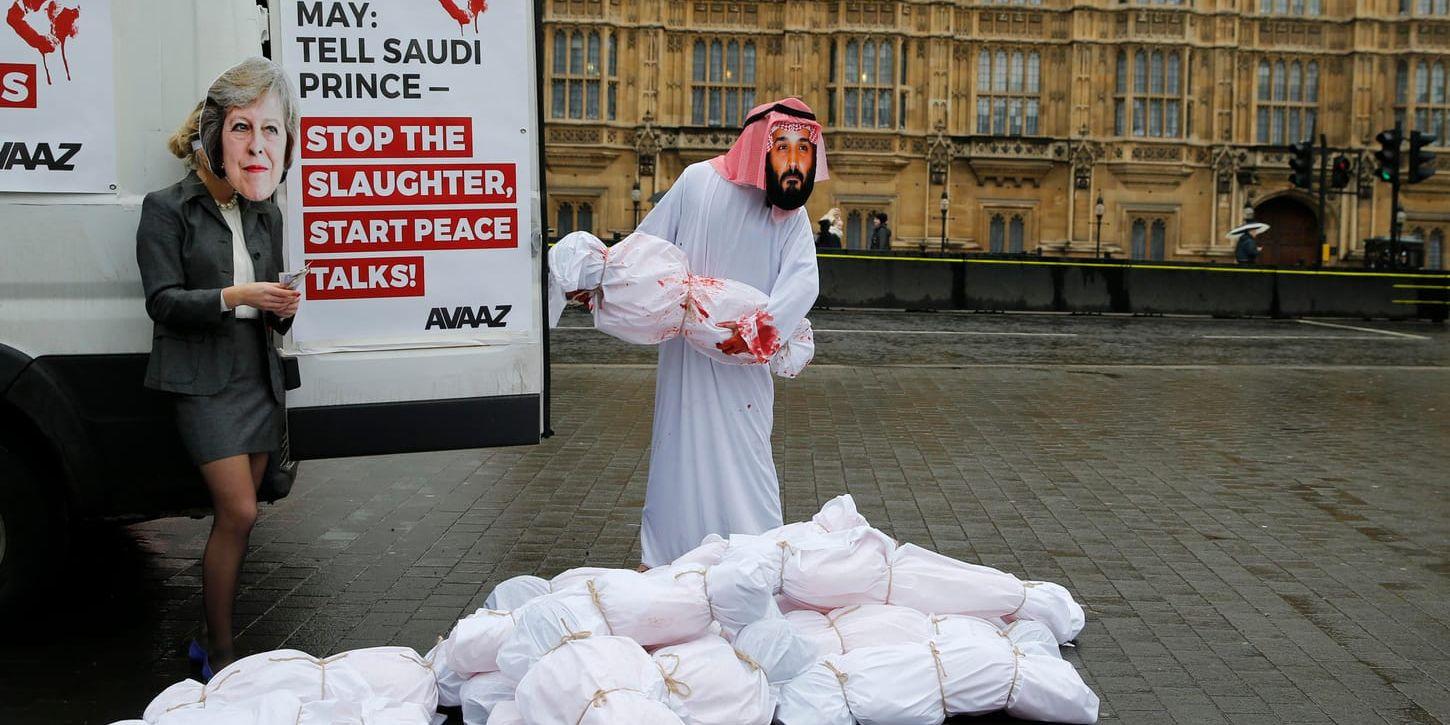Två demonstranter iförda masker föreställandes Storbritanniens premiärminister Theresa May (till vänster) och Saudiarabiens kronprins Mohammed bin Salman i London. På affischen står: "May: säg åt den saudiske prinsen att stoppa slakten, inleda fredssamtal".