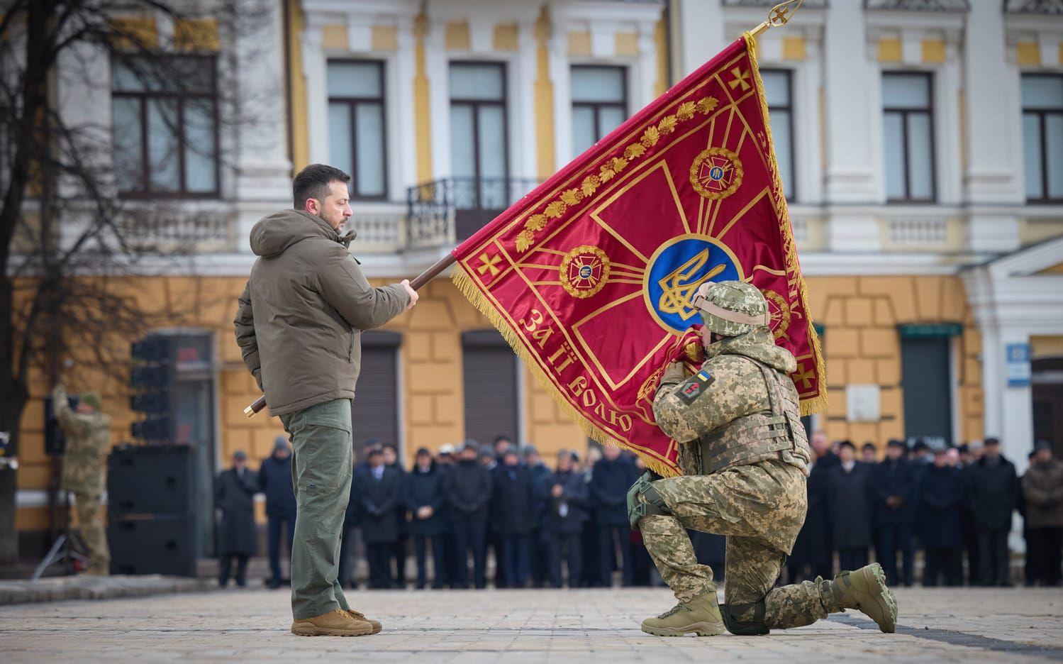 President Zelenskyj håller upp en militär flagga som en officer får kyssa, under fredagens årsdagsceremonier i Kiev.
