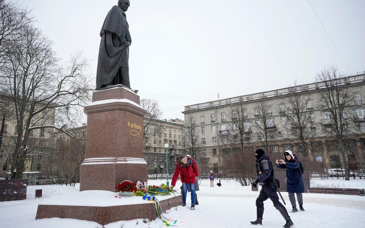 En polis på väg att gripa en man som lägger ner blommor vid en staty för den ukrainske poeten Taras Sjevtjenko i S:t Petersburg på fredagen.