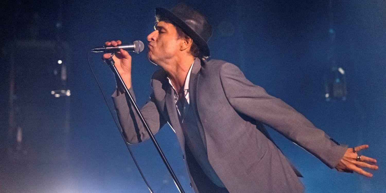 Thåström på scen i grå kavaj och hatt. 