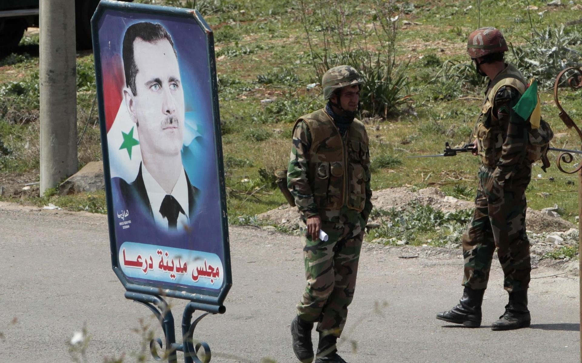 Syriska soldater vid ett porträtt av Bashar al-Assad. Kriget i Syrien har pågått i tio år. 