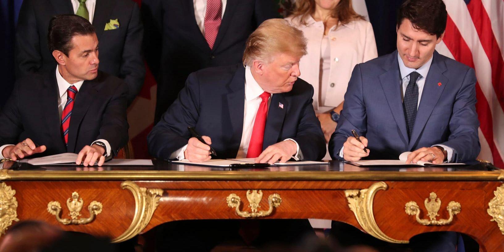 USA:s president Donald Trump, i mitten, ser på när Kanadas premiärminister Justin Trudeau skriver under det nya handelsavtalet. Mexikos president Enrique Pena Nieto till höger.