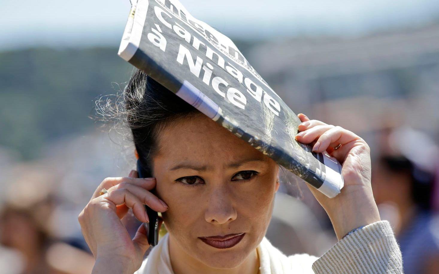 En kvinna tar skydd från solen på en gata i Nice. Tidningen förstasida handlar om massakern. Foto: TT