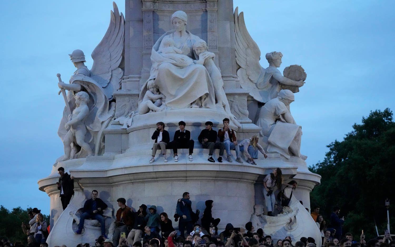 Folk har klättrat upp på Victoria Memorial-statyn utanför palatset. 