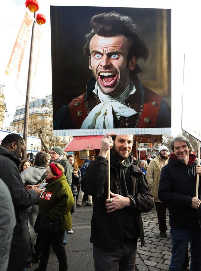 En man med nidbild av president Macron i demonstrationståget. Den franska presidenten vill höja pensionsåldern till 64 år från nuvarande 62 år.