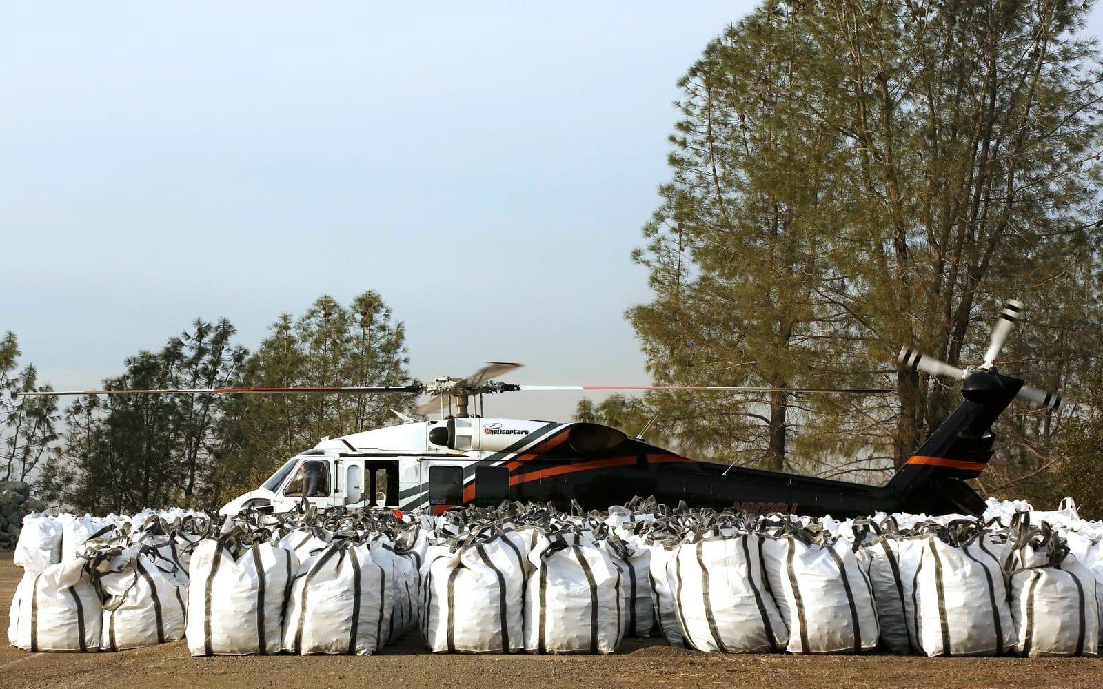 Helikoptrar står redo för att kunna droppa säckar med sten under arbetet med att säkra dammen. Bild: TT